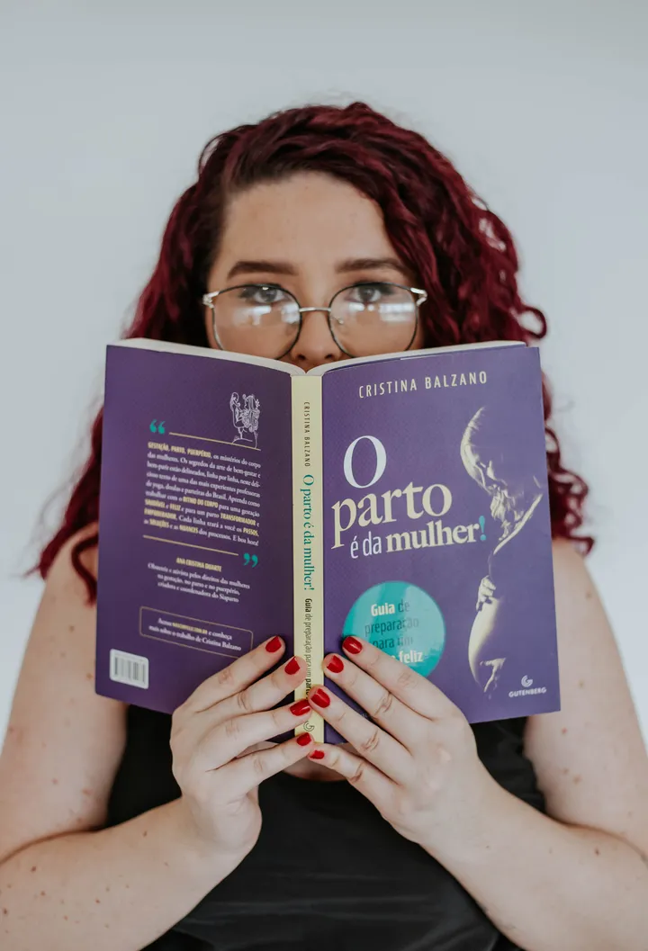 Rhavena Magna segurando aberto o livro O parto é da mulher, na frente do rosto
